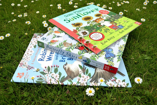 Three children's books on a grass lawn with daisies