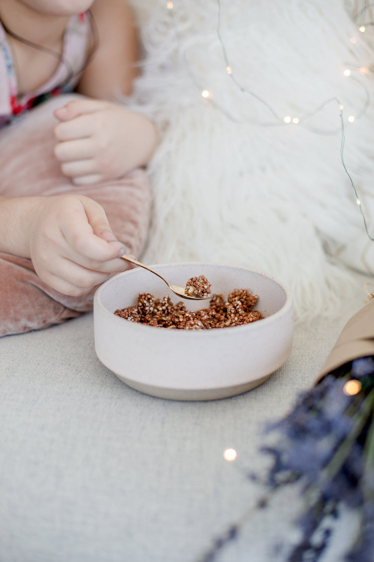 A child's hands hold a golden spoon with cereal on it over a white bowl | Photo by Farah