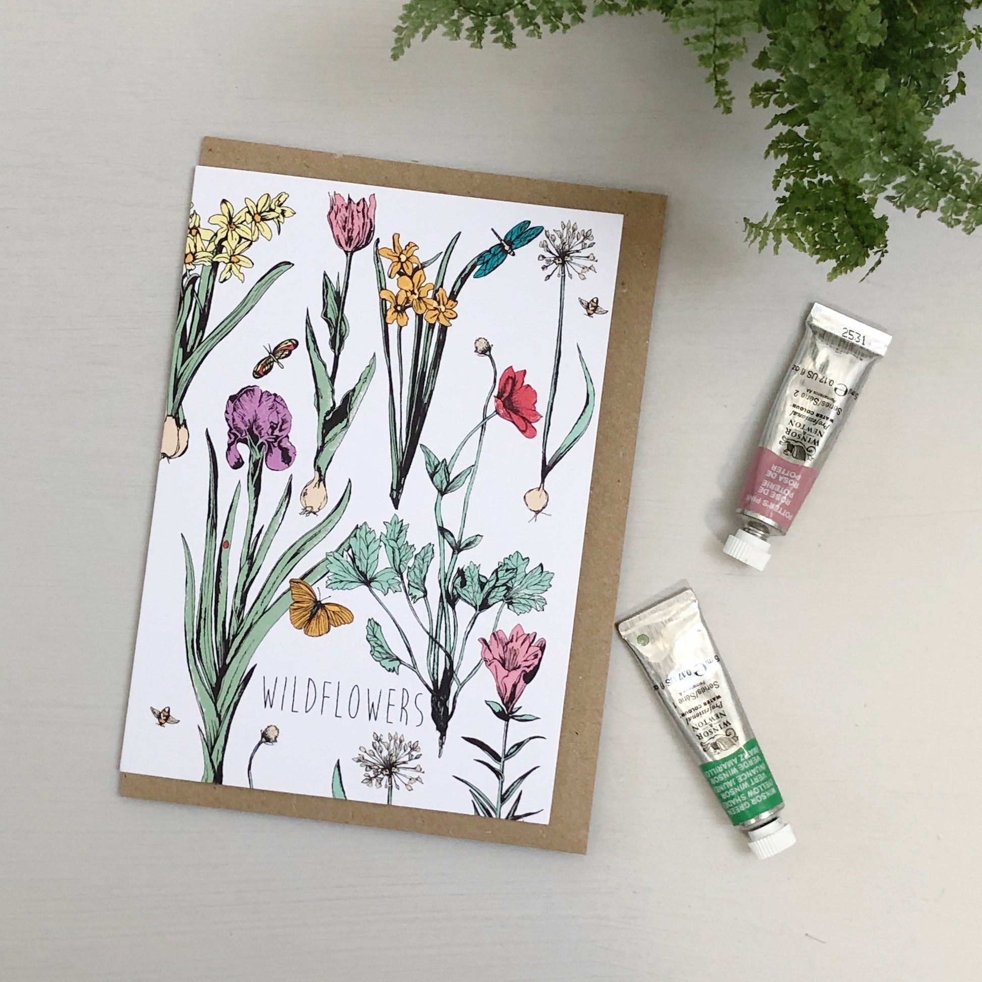 Card with wildflower illustration on a cream surface, with tubes of artist paints.