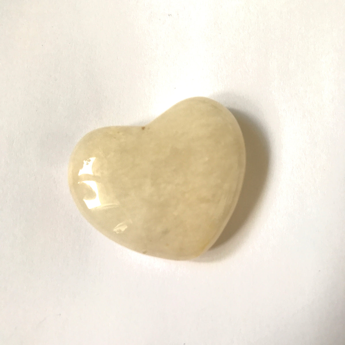A polished heart-shaped stone with a smooth, glossy finish, featuring natural marbled patterns in cream, resting on a plain white surface.