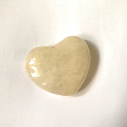 A polished heart-shaped stone with a smooth, glossy finish, featuring natural marbled patterns in cream, resting on a plain white surface.