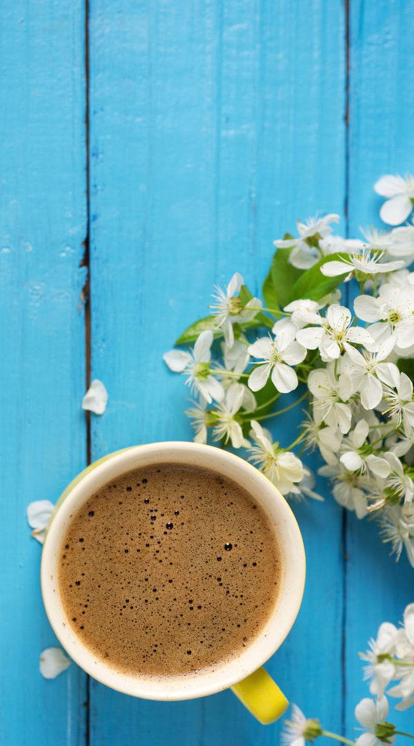 White mug with coffee on a blue wooden surface with white flowers