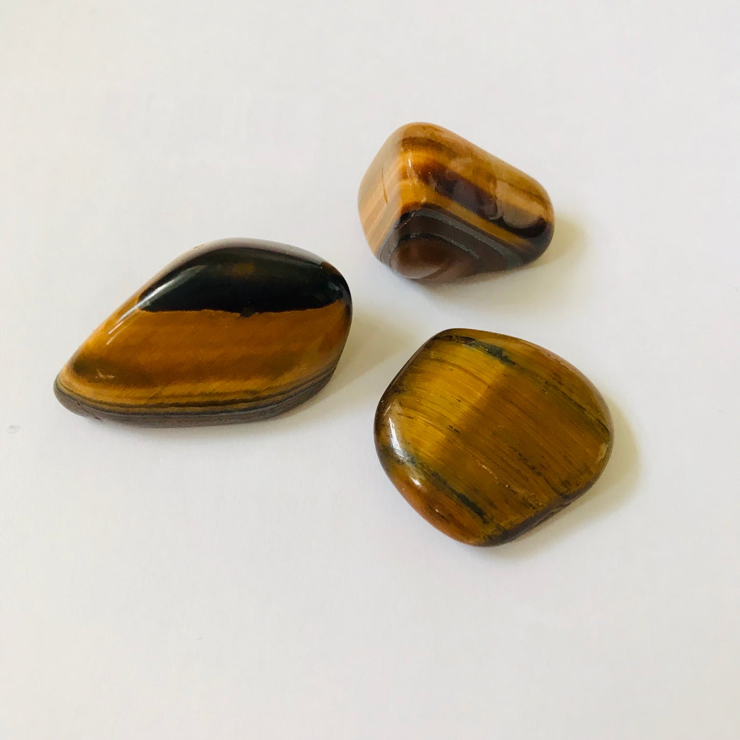Three polished tiger's eye stones with natural brown and black banded patterns, arranged on a plain white surface.
