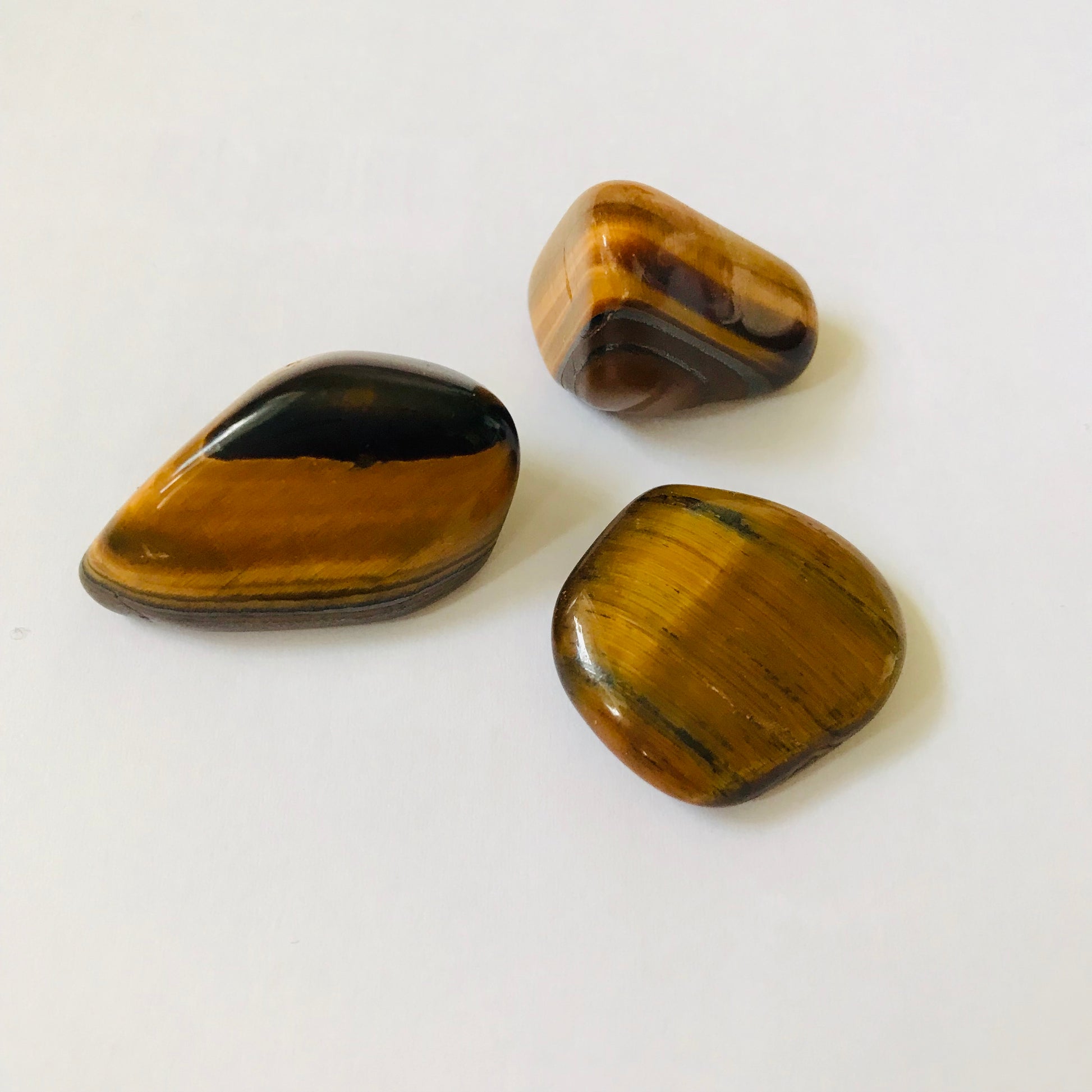 Three polished tiger's eye stones with natural brown and black banded patterns, arranged on a plain white surface.
