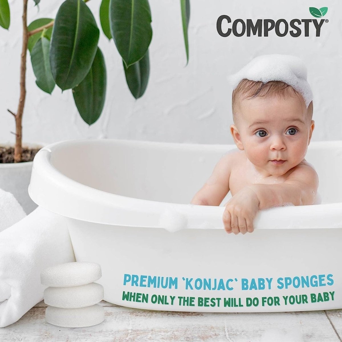 Baby in a bathtub with Composty premium konjac baby sponges and a plant in the background.