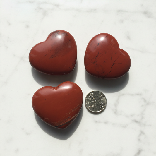 Three polished red heart-shaped stones arranged on a white textured surface