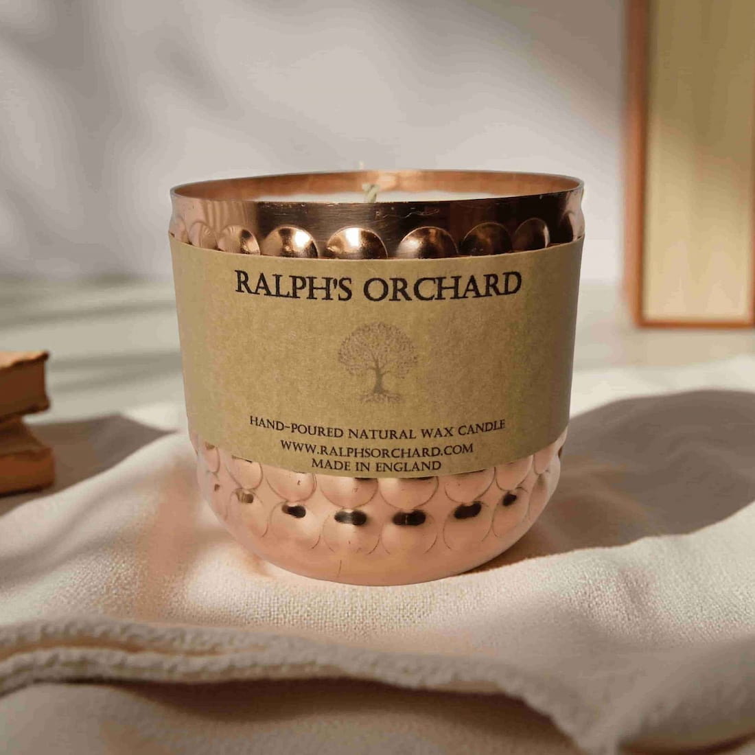 Candle in a decorative holder with 'Ralph's Orchard' branding on a soft background