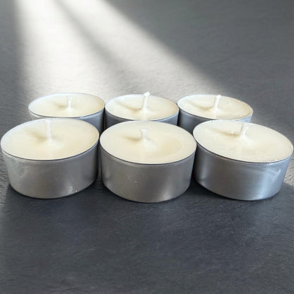 Six small white candles in metal holders on a dark surface
