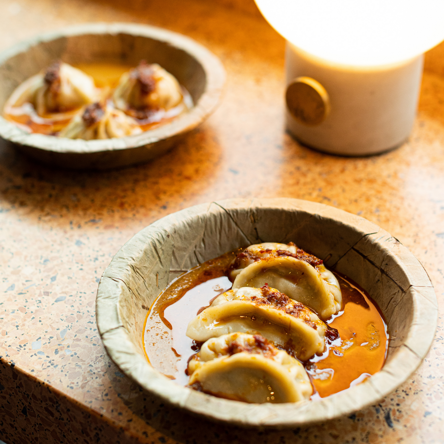 Dumplings in a leaf bowl on a textured surface with a cup in the background