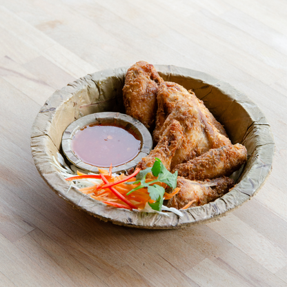 Fried chicken wings with a side of sauce and vegetables on a leaf plate.