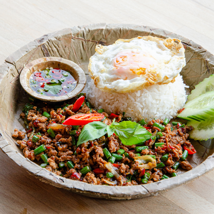 Plated leaf dish with rice, ground meat, vegetables, and a fried egg on a wooden surface.