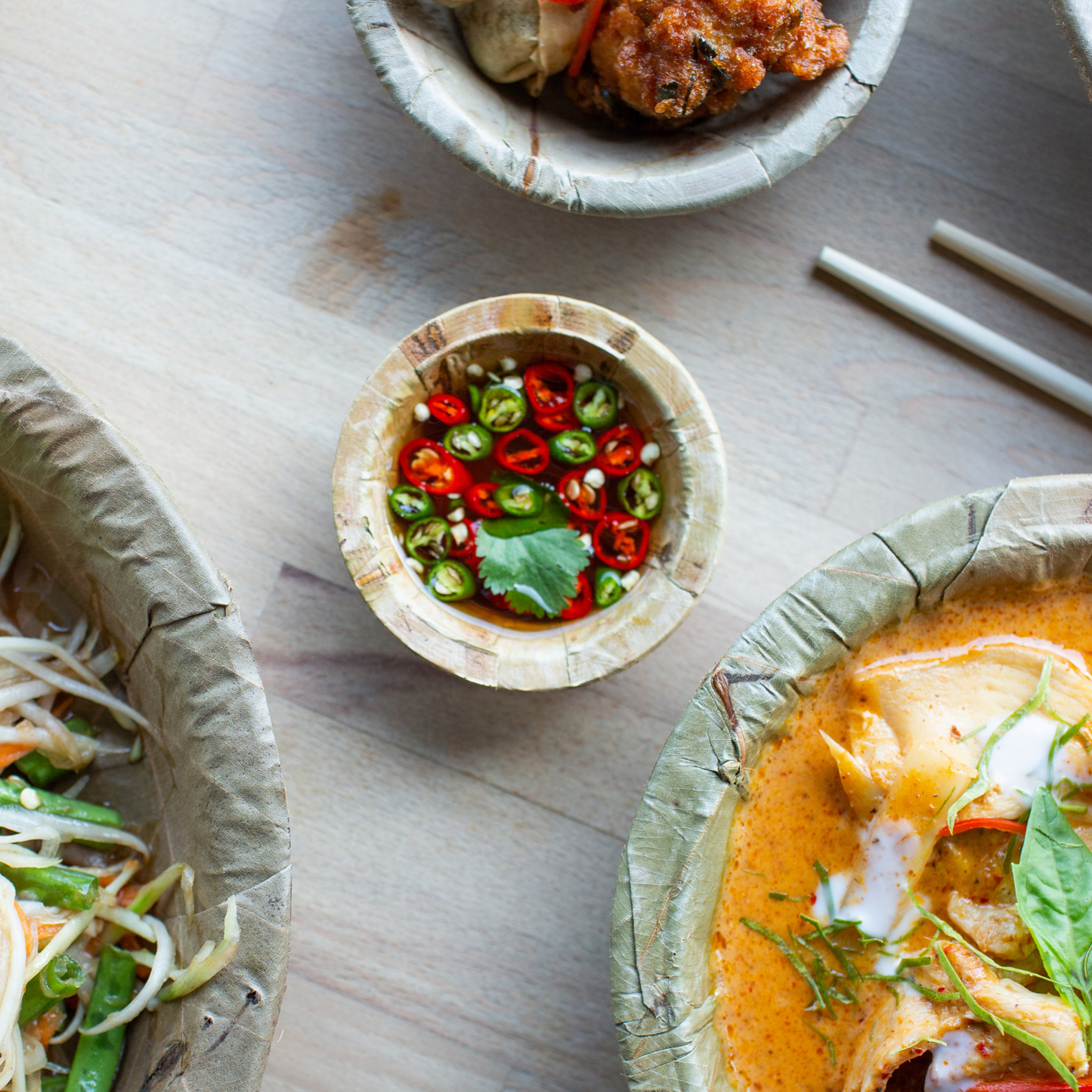 Assorted Tapri sal leaf dishes, including a bowl of soup, a salad, and a small bowl of chilli peppers on a wooden surface.