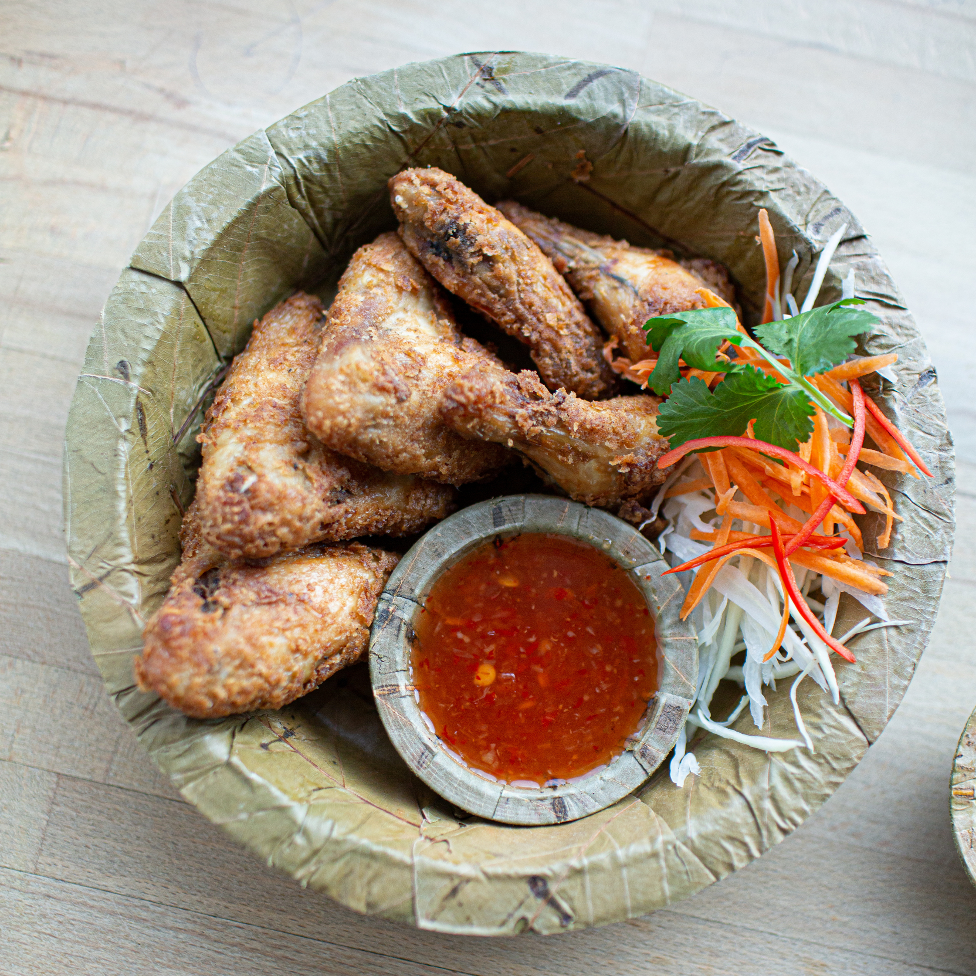 Fried chicken wings with a side of sauce and vegetables on a Tapri sal leaf plate.