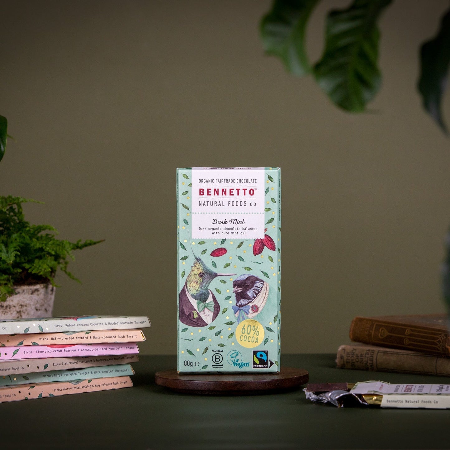 Bennetto natural foods chocolate bar packaging on a wooden stand with books and plants in the background