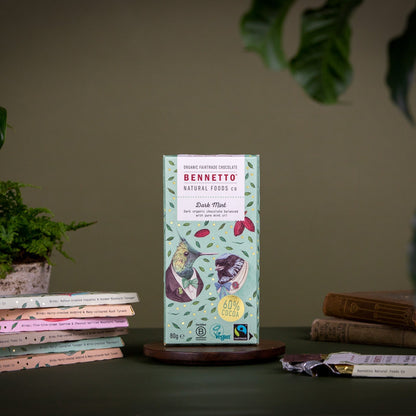 Bennetto natural foods chocolate bar packaging on a wooden stand with books and plants in the background